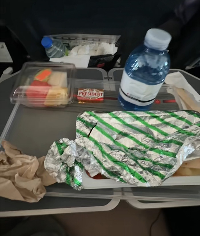 Comida servida en vuelo de Air Canada con agua y alimentos empaquetados en bandeja durante crítica de pasajera. Comida servida en vuelo de Air Canada con agua y alimentos empaquetados en bandeja durante crítica de pasajera.