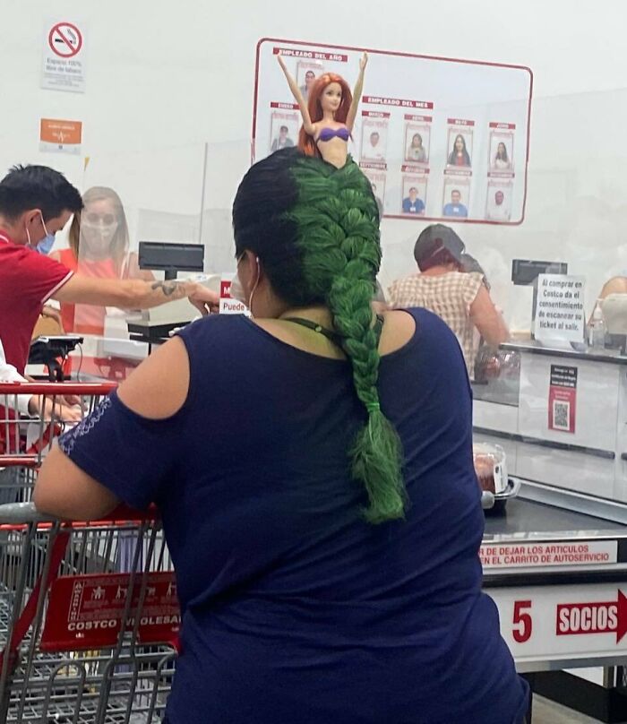 Mujer en Walmart con trenza verde adornada con muñeca pelirroja, imagen única para fotos sorprendentes en Walmart.
