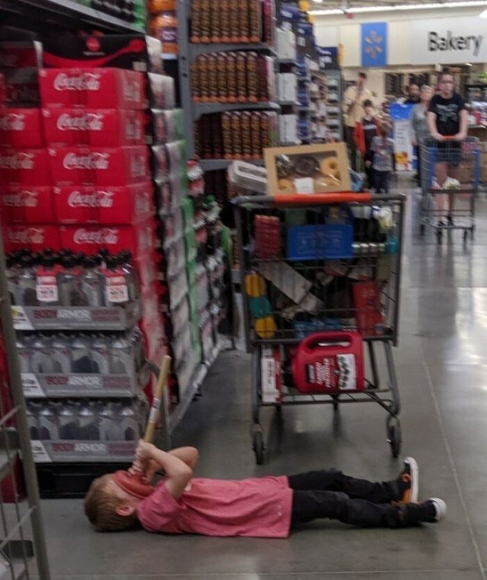 Niño acostado en el suelo del pasillo de Walmart con un bate, imagen inesperada en tienda Walmart para SEO.