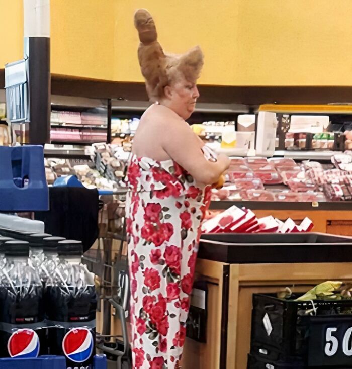 Mujer en Walmart con vestido de flores y peinado extravagante mientras compra en la sección de carnes.
