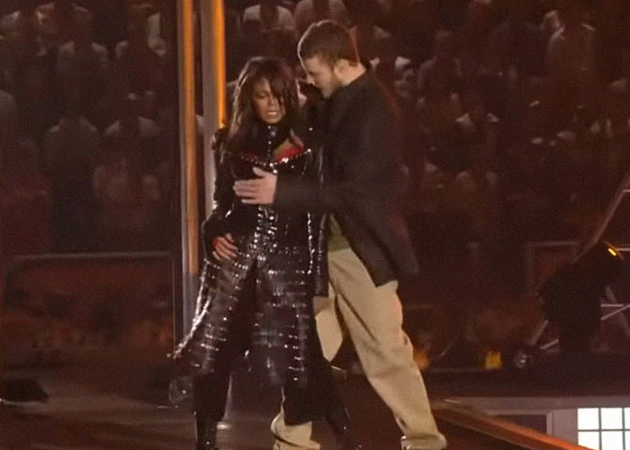 Momento de traición en Hollywood durante evento nocturno con artistas en el escenario y público en el fondo.