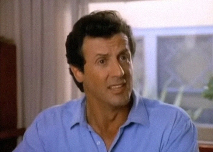 Hombre en camisa azul gesticulando, ilustrando momentos de traición y backstabbing en Hollywood, expresión de sorpresa.