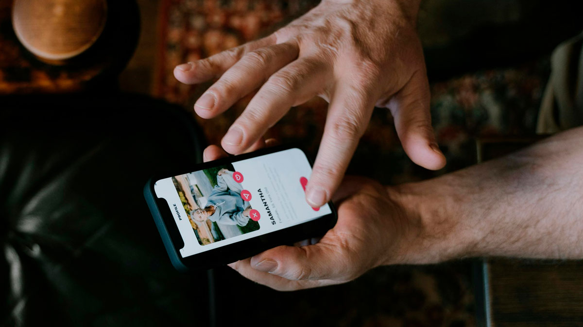 Hombre usando un telu00e9fono mu00f3vil para revisar perfiles en una app, ilustrando la venganza contra ex parejas.