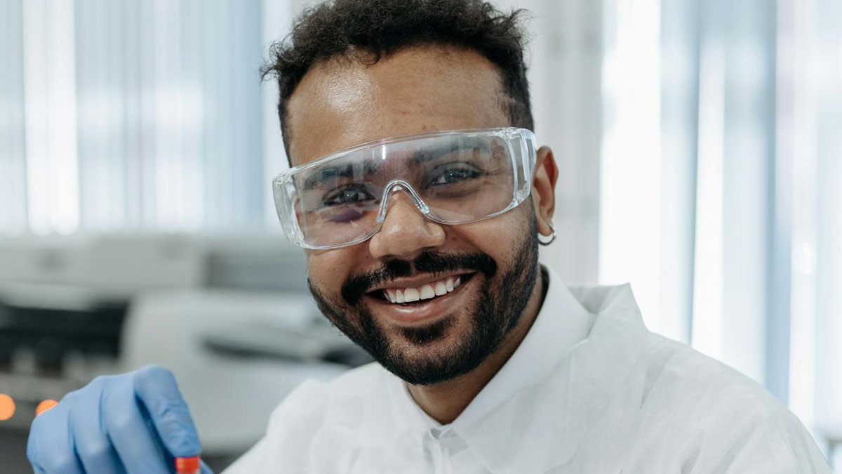 Hombre sonriente con gafas de seguridad y bata en laboratorio, ilustrando cosas ingeniosas y divertidas dichas en el momento.