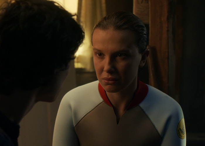 Millie Bobby Brown en Stranger Things con expresión tensa y luz dramática, escena que captura la atención de los fans.