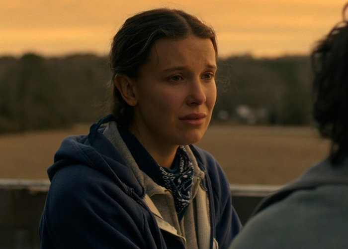 Millie Bobby Brown en escena emotiva de Stranger Things durante una conversación al aire libre en hora dorada.