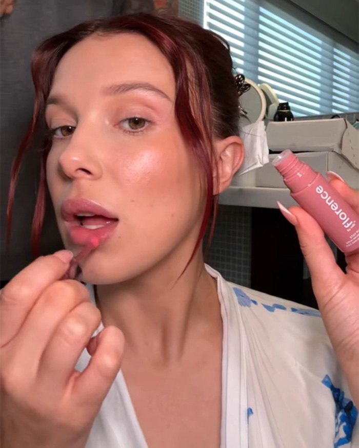 Millie Bobby Brown aplicando brillo labial en primer plano, fans atentos a su aparición en Stranger Things viralizada.