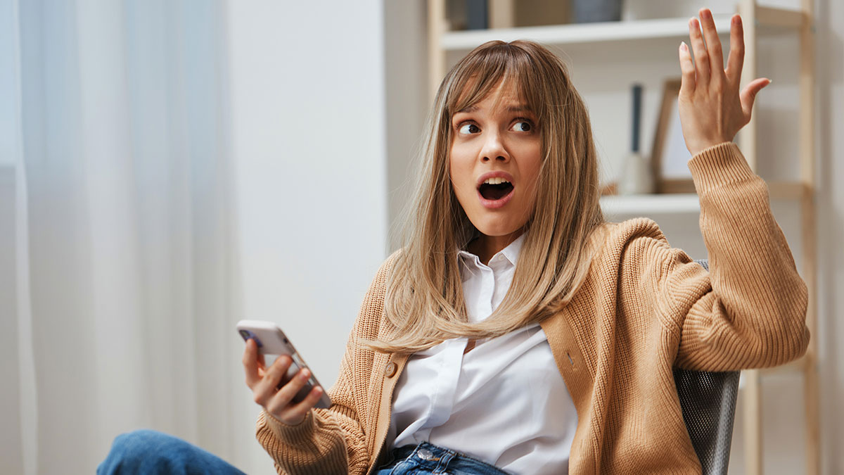 Mujer sorprendida y confundida leyendo mensajes de texto divertidos que tomaron un giro inesperado en su telu00e9fono mu00f3vil.