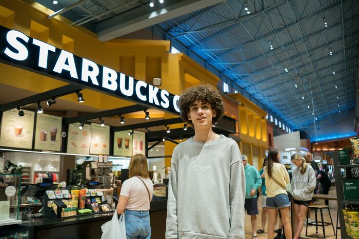 Joven en Starbucks mostrando una expresión que refleja experiencias de instant karma y manifestaciones satisfactorias en público.