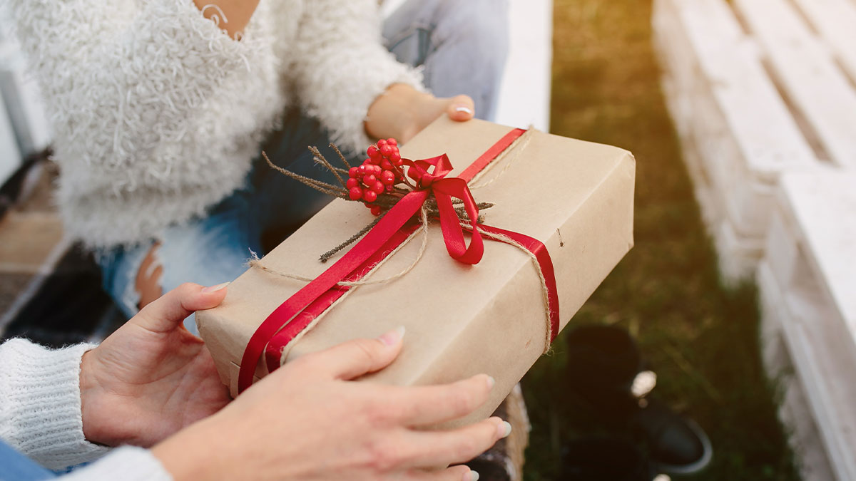 Persona entregando un regalo envuelto con cinta roja y decoraciu00f3n festiva, idea perfecta para intercambios white elephant.