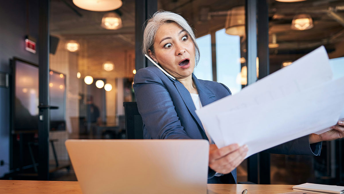 Mujer de negocios sorprendida en oficina mientras sostiene documentos y habla por telu00e9fono sobre escu00e1ndalos laborales.