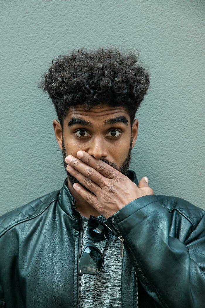 Hombre sorprendido con chaqueta de cuero y cabello rizado mostrando una reacción divertida y aguda en el momento.