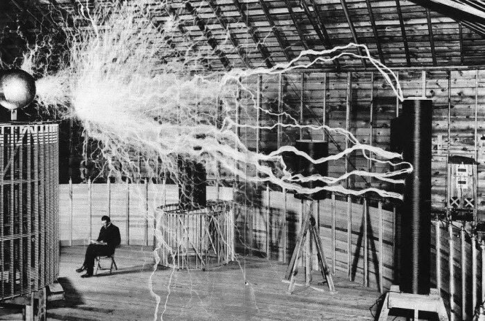 Hombre sentado cerca de un generador eléctrico antiguo con descargas eléctricas en laboratorio histórico, fotos antiguas únicas.