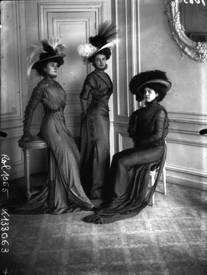 Tres mujeres con vestidos y sombreros antiguos posan en una habitación elegante en fotos antiguas que nunca veremos en la vida real.