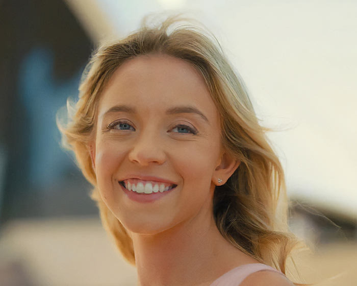 Sydney Sweeney sonriente al aire libre mostrando su belleza natural con luz suave y fondo desenfocado como evidencia fans.