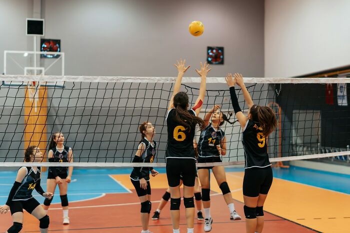 Equipo femenino de voleibol bloqueando el balón en partido competitivo representando manifestaciones de karma instantáneo.
