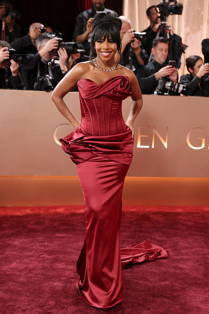 Mujer sonriente en vestido rojo elegante en la alfombra roja, uno de los outfits de los Golden Globes que impactaron a fans.