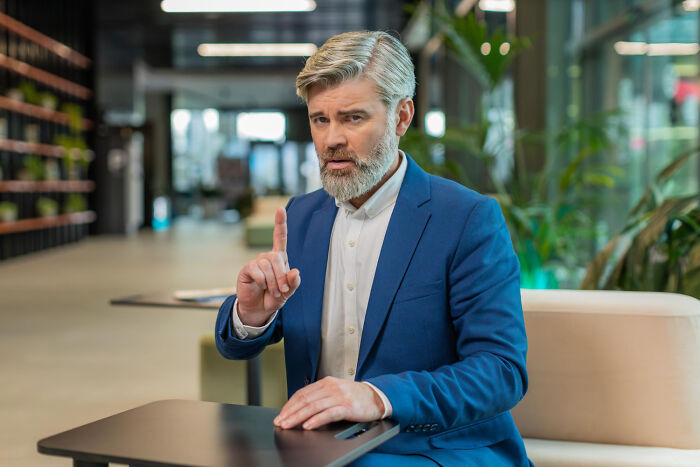 Hombre con traje azul mostrando gesto de aviso en oficina moderna, simbolizando momentos de decir no es mi problema.