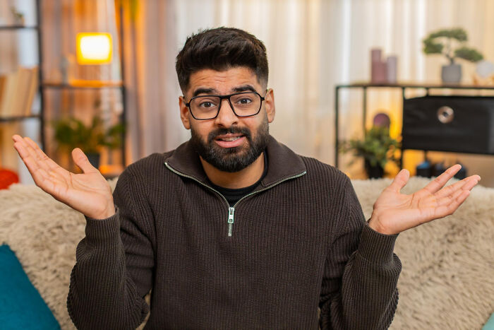 Hombre con gafas y suéter marrón mostrando expresión de indiferencia simbolizando momentos de no es mi problema más.