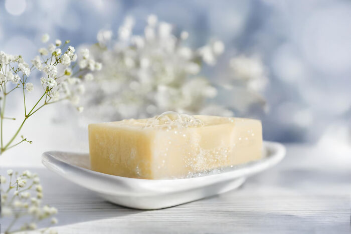 Jabón con burbujas sobre una jabonera blanca rodeada de flores blancas, mostrando momentos de dejar problemas atrás.