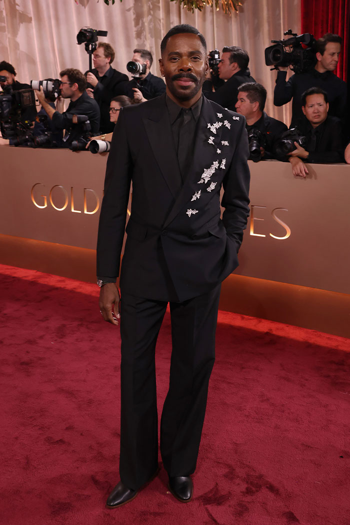 Hombre vestido con traje negro decorado en hombro en la alfombra roja mostrando outfits Golden Globes que impactaron fans.