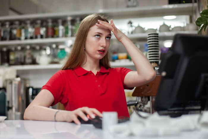 Mujer en restaurante con camiseta roja muestra frustración y actitud de no ser su problema mientras usa computadora.