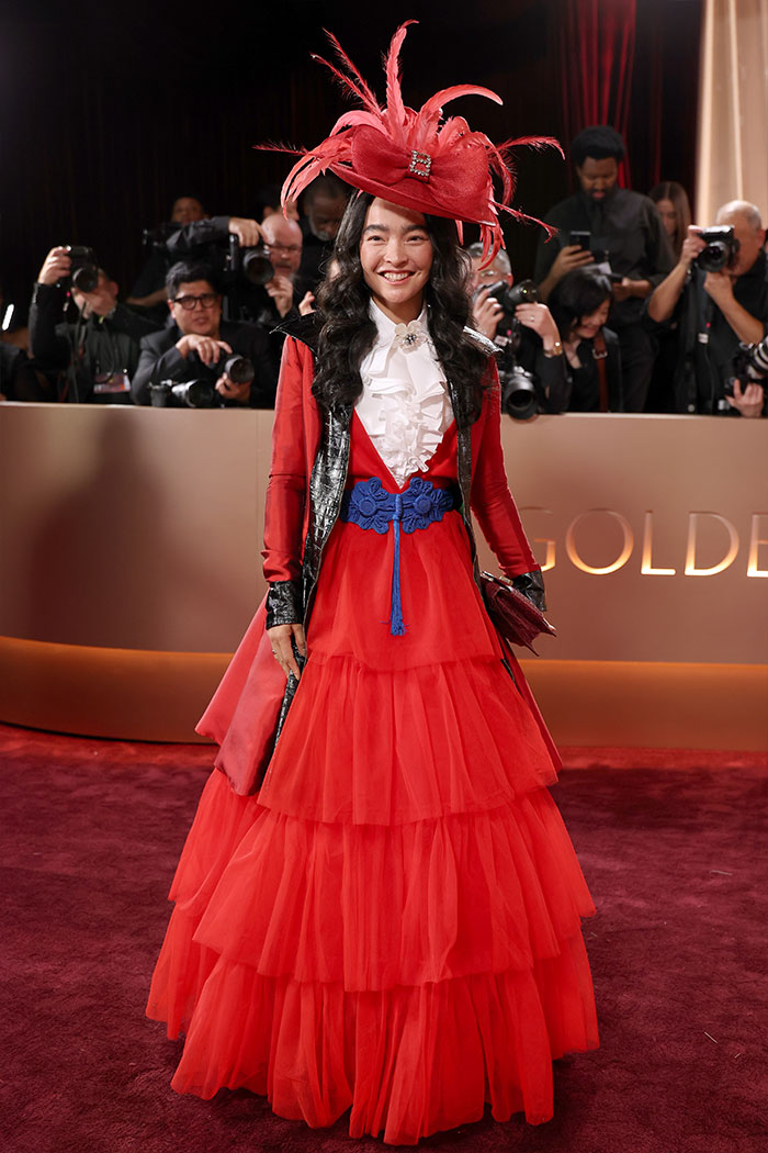 Mujer con vestido rojo y sombrero extravagante en alfombra roja, destacando desastres de moda en los Golden Globes 2026.