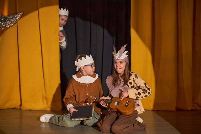 Niños actuando en teatro con coronas, uno tocando ukelele, mostrando momentos de decir no es mi problema y marcharse.
