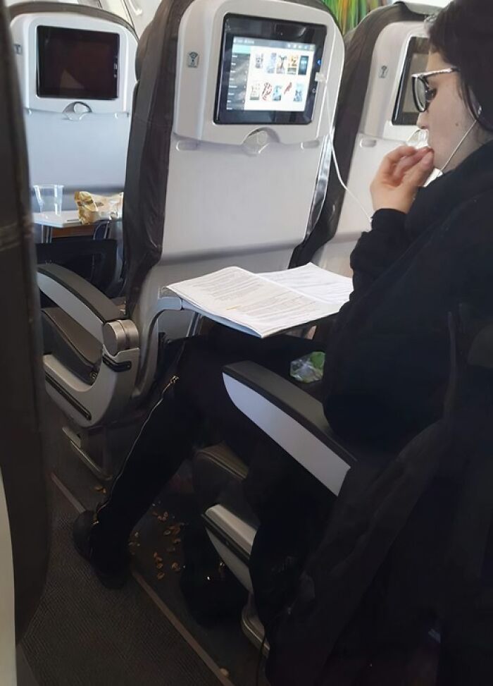Persona fumando y tirando desperdicios en el suelo de un avión, comportamiento que muestra ser un jerk en espacios públicos.