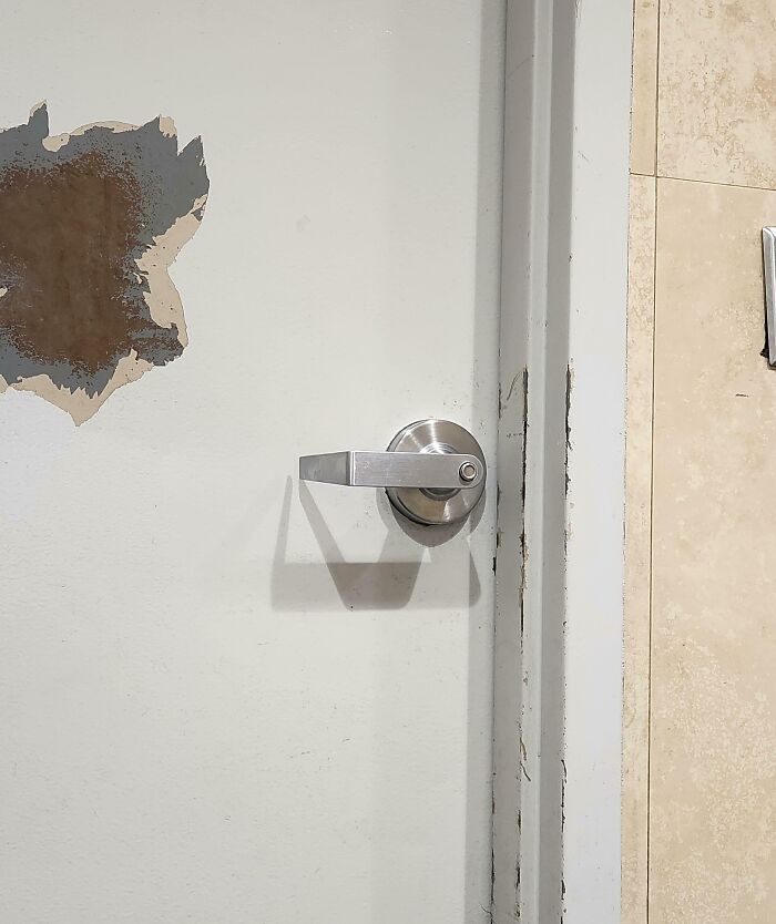 Manija de puerta dañada y pared con pintura descascarada en espacio público, ejemplo de comportamiento molesto online.