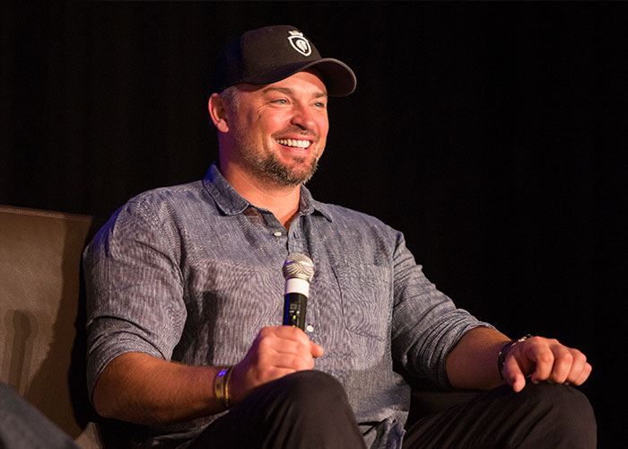 Hombre sonriente con gorra y camisa casual, hablando en panel sobre galanes adolescentes de los 2000 y su apariencia actual.