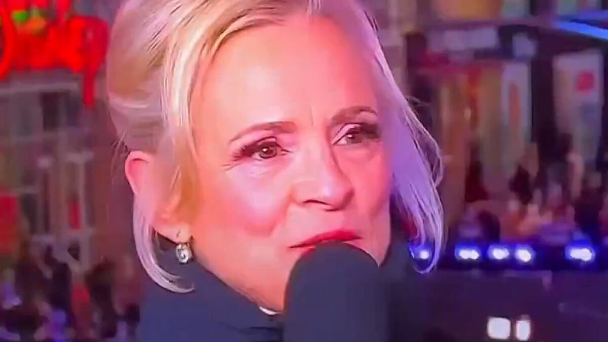 Actriz en la vu00edspera de Au00f1o Nuevo hablando al micru00f3fono, rostro iluminado y pu00fablico desconcertado tras comentario transfu00f3bico