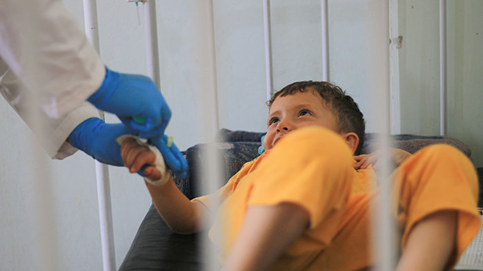 Niño acostado en cama sonriente mientras recibe atención médica, mostrando comportamiento que sugiere inteligencia inquietante.