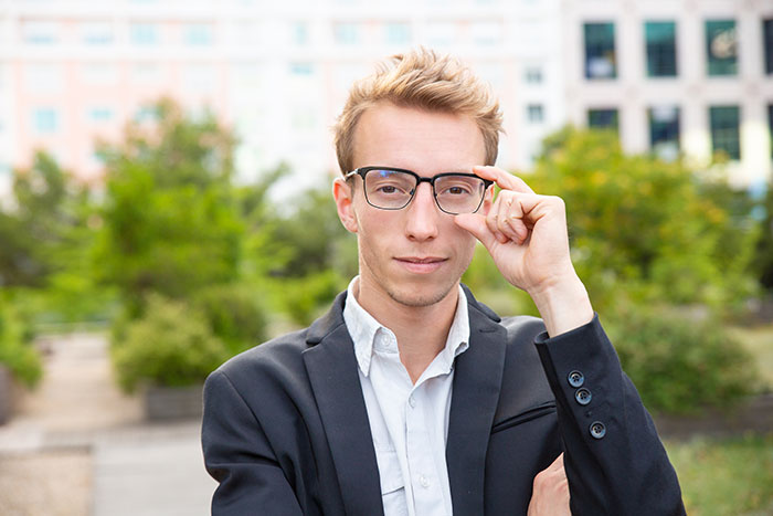 Joven con gafas y saco negro en exteriores, representando un ejemplo de la inteligencia inquietante que impacta a otros.