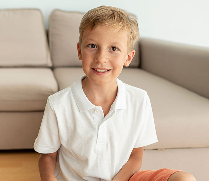 Niño sonriente sentado en sala, mostrando una expresión que refleja inteligencia y curiosidad excepcionales.