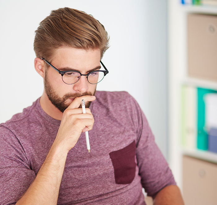 Hombre joven con gafas pensativo, muestra una expresión que refleja creencias y displays de inteligencia inquietante.