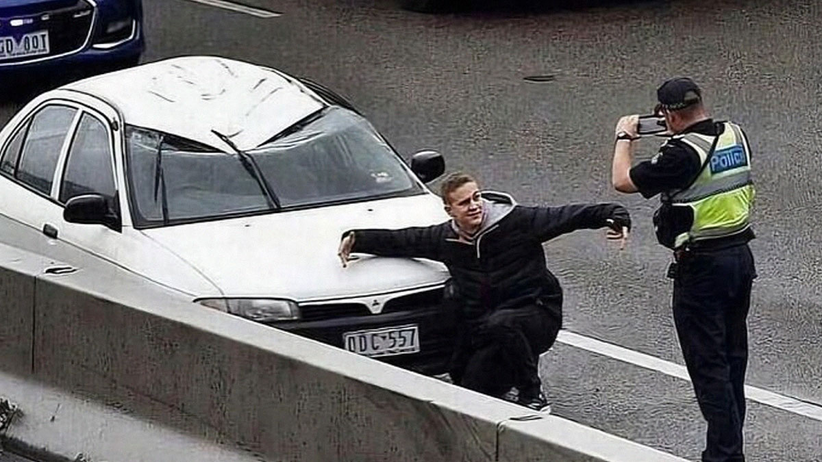 Hombre posando junto a coche con techo aplastado mientras policu00eda toma foto, imagen horrible pero divertida que incomoda.