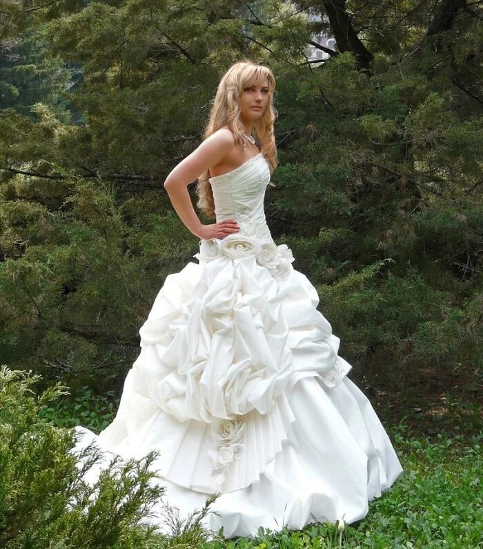 Novia con vestido de boda blanco detallado posando en jardín rodeada de naturaleza, reflexión sobre compra de vestidos de boda.